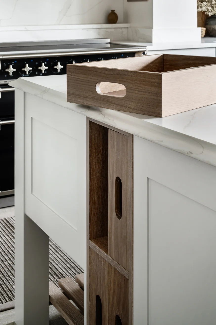 Wooden serving tray on a white marble kitchen island with built-in wood cubby storage and a stove in the background.
