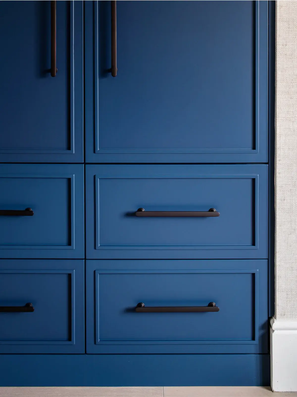 Blue paneled cabinet drawers with dark horizontal bar handles and decorative molding against a light wall and baseboard.
