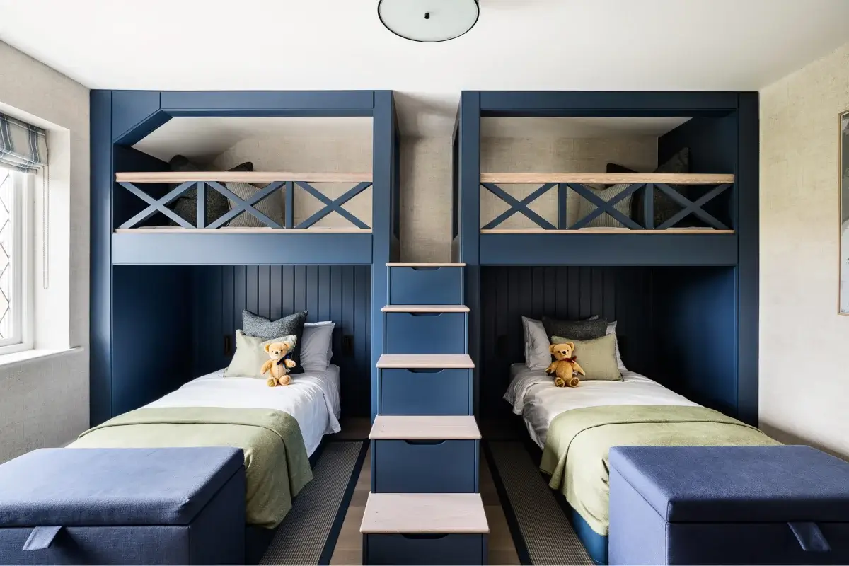 Symmetrical kids' bedroom with navy built-in bunk frames, twin beds below, ladder of drawers between them, teddy bears on each bed