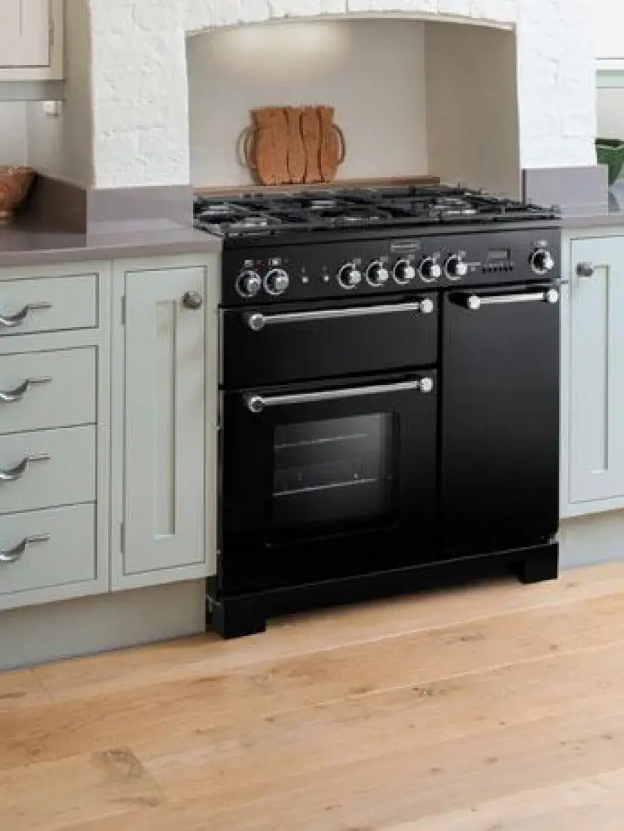 Black freestanding gas range with double oven and stainless knobs set between light gray kitchen cabinets on wood floor.